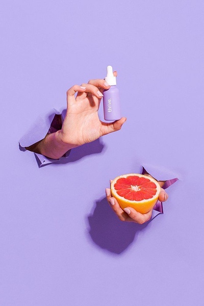 A clean, high-contrast product hero shot featuring a purple serum bottle and a sliced grapefruit against a vibrant purple background.